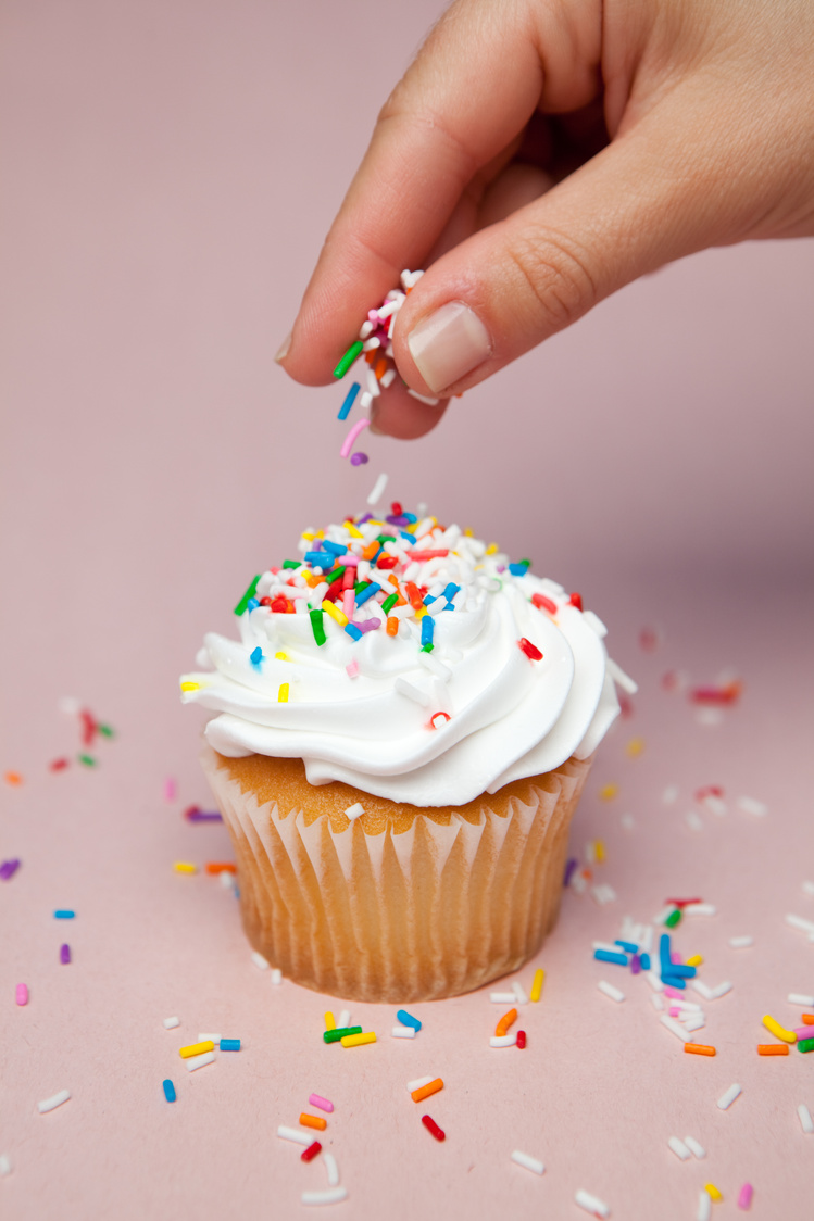 sprinkling sprinkles on cupcake